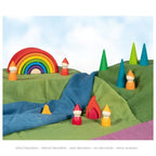Colorful wooden toy landscape with rainbow, trees, and small figures on a green and blue fabric background.