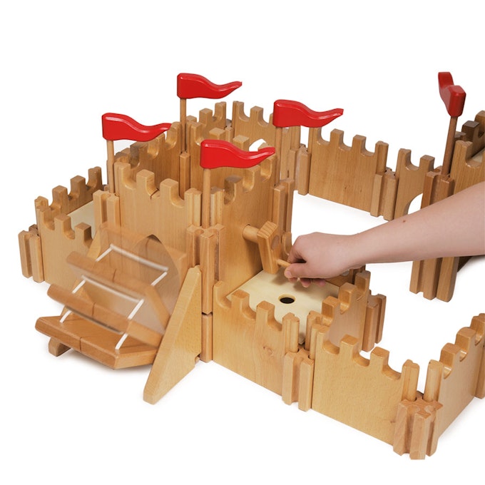Wooden toy castle with red flags and a hand interacting with it on a white background